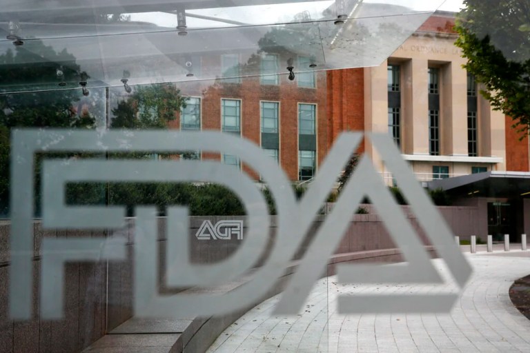 This Aug. 2, 2018, file photo shows the U.S. Food and Drug Administration building behind FDA logos at a bus stop on the agency's campus in Silver Spring, Maryland. Regulators warned several companies to stop selling soaps, sprays and other concoctions with false claims that they can treat COVID-19 or keep people from catching it. The warnings were emailed Friday, March 6, 2020, to companies based in the United States, Canada, and the United Kingdom and were announced Monday. Nearly all the targeted companies had complied by Monday morning, with mentions of the virus or products to treat it taken off their websites.